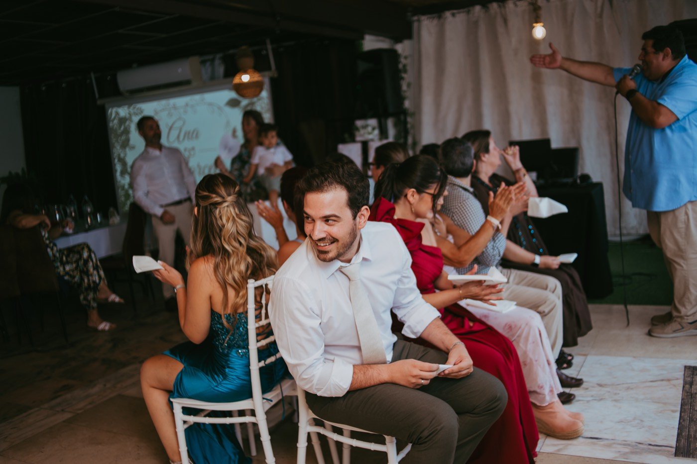 Os convidados sentados em fila num dos jogos da festa, a rir.
